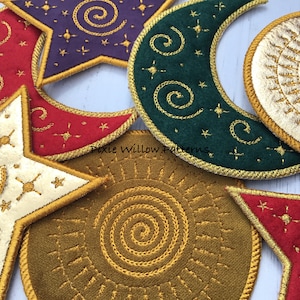 May include: Five felt ornaments in the shape of a star, crescent moon, and sun. The ornaments are embroidered with gold thread in a spiral pattern. The ornaments are on a white surface. The text "Pixie Willow Patterns" is visible in the image.