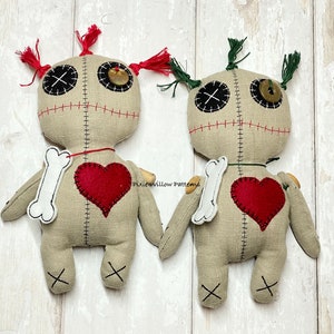 May include: Two handmade voodoo dolls with red and green yarn hair, stitched mouths, button eyes, and red felt hearts. Each doll holds a white felt bone.