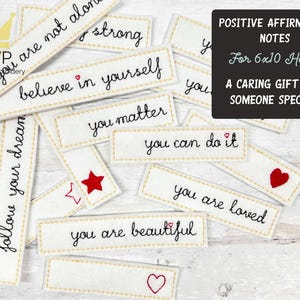 May include: A collection of white rectangular embroidered patches with positive affirmations in black script, such as "believe in yourself" and "you are loved." Some patches feature red heart and star designs. A black sign reads "Positive Affirmation Notes for 6x10 Hoops."