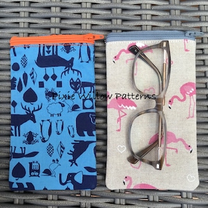 Pode incluir: Duas bolsas com zíper para óculos, uma com fundo azul e um padrão de animais e formas geométricas, a outra com fundo bege e um padrão de flamingos cor-de-rosa. O texto "Pixie Willow Patterns" é visível na bolsa com o padrão de flamingos.