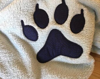 May include: A light blue, plush blanket featuring a large, dark blue paw print design. The paw print is centered on the blanket and has a textured appearance. The blanket is made of a soft, fuzzy material.