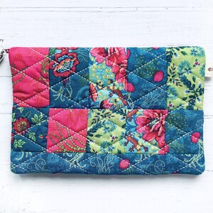 May include: A quilted fabric pouch with a patchwork design featuring pink, green, and blue floral patterns. The pouch has a zipper closure and a small tassel.