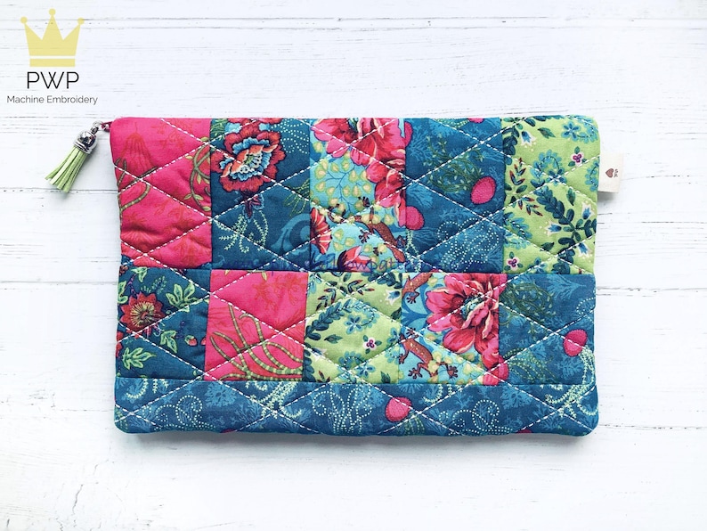 May include: A quilted fabric pouch with a patchwork design featuring pink, green, and blue floral patterns. The pouch has a zipper closure and a small tassel.