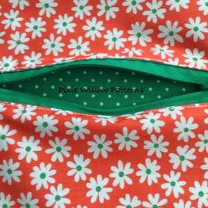 Puede incluir: Primer plano de una tela con estampado floral y un bolsillo con cremallera. La tela es naranja con margaritas blancas y centros verdes. El bolsillo es verde con lunares blancos y el texto "Pixie Willow Patterns".