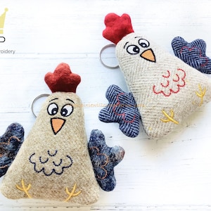 May include: Two embroidered felt chicken keychains. One is red, white, and blue with a blue and white checkered pattern. The other is brown, white, and red with a blue and white checkered pattern. Both have black eyes and yellow beaks.