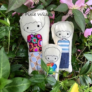 May include: Three handmade fabric dolls with embroidered faces and clothing. The dolls are in a garden setting with green foliage and pink flowers. The text "Pixie Willow Patterns" is visible.