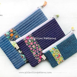 May include: Three quilted zipper pouches in different sizes. The largest pouch is blue denim with a floral print panel. The middle pouch is dark blue with a pink floral print panel. The smallest pouch is teal blue with a floral print panel. All pouches have white zippers and a tassel pull.