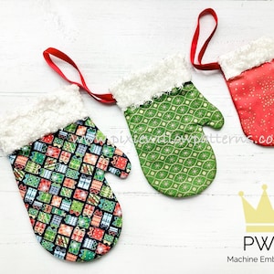 May include: Three Christmas mitten ornaments with different fabric patterns. The mittens are red with gold glitter, green with a white and gold pattern, and black with a colourful gift print. Each mitten has a white faux fur cuff and a red ribbon loop.