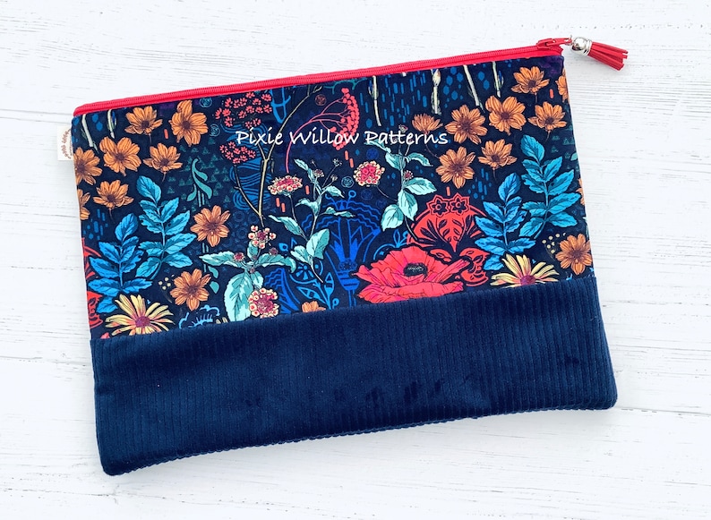 Op de afbeelding: Een blauwe ritszak met een bloemenprint en een donkerblauwe corduroy bodem. De tas heeft een rode rits en een zilveren kwast. De tekst "Pixie Willow Patterns" is op de tas gedrukt.