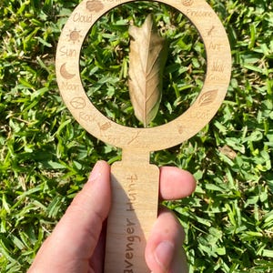 May include: Wooden magnifying glass with a scavenger hunt theme. The magnifying glass has a circle with various nature items listed around the edge, including a worm, flower, pinecone, ant, grass, leaf, bird, spider, and rock. The handle of the magnifying glass says "Scavenger Hunt".