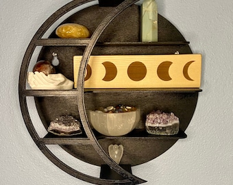 May include: A black wooden crescent moon shelf with five shelves. The shelves are decorated with crystals, stones, and a wooden sign with five moons.