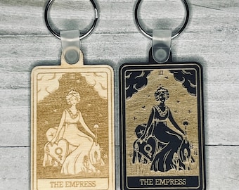 May include: Two wooden keychains featuring the Empress tarot card. One keychain is natural wood with a light brown finish and the other is black with a gold finish. Both keychains feature the Empress card with a woman sitting on a throne with a heart and a crown.