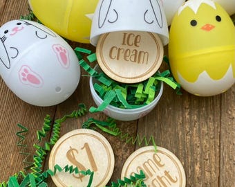 May include: A set of plastic Easter eggs with different designs, including a bunny, a chick, and a plain yellow egg. Each egg contains a wooden circle with a different message, including "Ice Cream", "Game Night", and "$1".