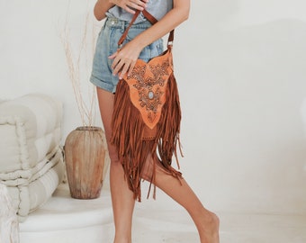 May include: A brown leather crossbody bag with fringe detailing and intricate floral carvings. The bag has a flap closure and a turquoise stone embellishment.