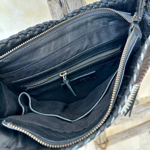 May include: Black leather handbag with a braided design and a zipper closure. The bag has a black lining and a zippered pocket inside.