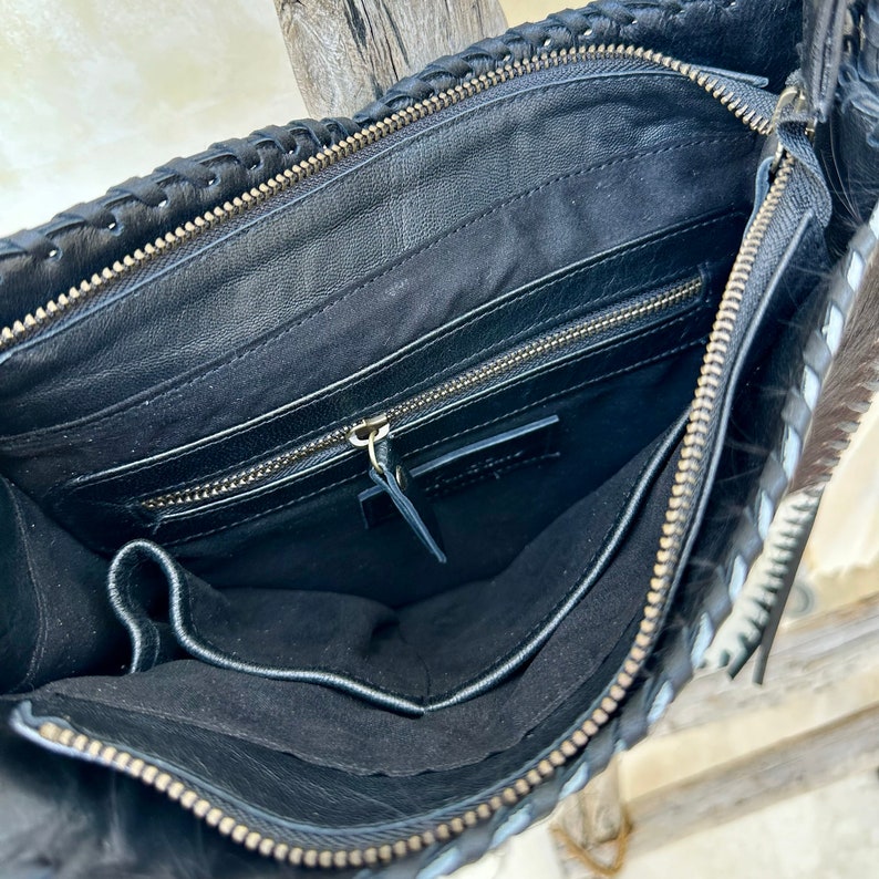 May include: Black leather handbag with a braided design and a zipper closure. The bag has a black lining and a zippered pocket inside.