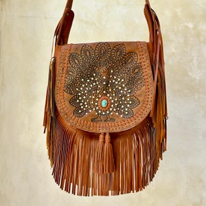 May include: A brown leather shoulder bag with a peacock design and fringe. The peacock is embellished with rhinestones and a turquoise stone.