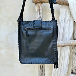 May include: Black leather crossbody bag with a flap closure and a zippered pocket on the back. The bag has a fringe detail on the bottom.