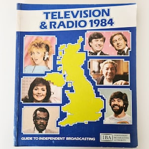 Könnte beinhalten: Ein blauer Buchumschlag mit dem Titel "Fernsehen & Radio 1984" und dem Text "Guide to Independent Broadcasting" darunter. Der Umschlag zeigt eine gelbe Karte des Vereinigten Königreichs und Fotos von sechs Personen.