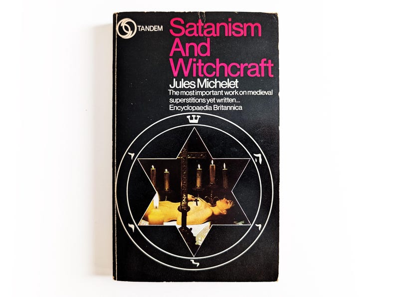 May include: A vintage paperback book titled "Satanism And Witchcraft" by Jules Michelet. The cover is black with pink and white text and a white pentagram design. The book is a historical work on medieval superstitions.
