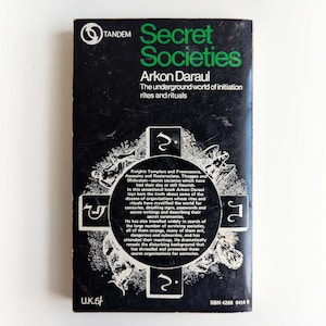 May include: Black and white book cover with green text that reads "Secret Societies" by Arkon Daraul. The subtitle reads "The underground world of initiation rites and rituals". The cover features a cross with symbols and illustrations.