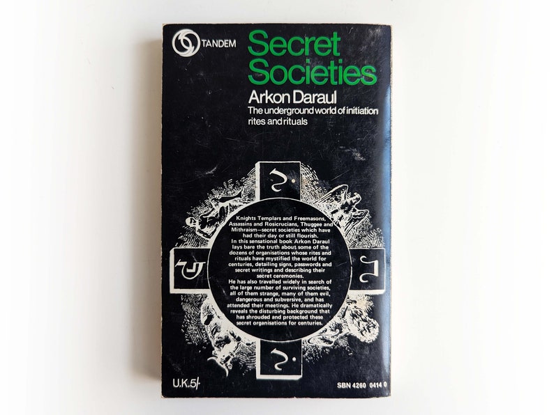 May include: Black and white book cover with green text that reads "Secret Societies" by Arkon Daraul. The subtitle reads "The underground world of initiation rites and rituals". The cover features a cross with symbols and illustrations.
