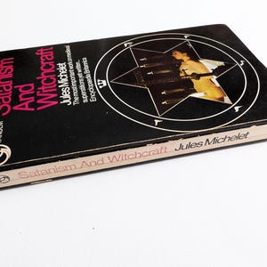 May include: A vintage copy of "Satanism And Witchcraft" by Jules Michelet. The book has a black cover with white and pink lettering, and a pentagram design. Published by Tandem, it is a historical work.