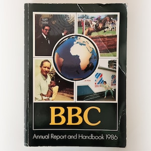 Może przedstawiać: Czarna i zielona książka z tekstem "BBC Annual Report and Handbook 1986" na okładce. Okładka zawiera kolaż obrazów, w tym globus, mężczyznę trzymającego dziecko, mężczyznę w garniturze, konia skaczącego przez płot i ciężarówkę z logo stacji radiowej.