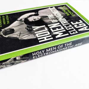 May include: A hardcover book titled Holy Men of the Electromagnetic Age by Raphael Cormack. The cover features a black and white photograph of a person in traditional headwear, framed by a bright green border with the text A Forgotten History of the Occult.