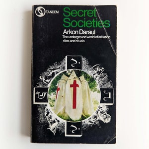 May include: A black and white book cover with the title "Secret Societies" in green letters. The subtitle is "Arkon Daraul The underground world of initiation rites and rituals". The cover features a black and white illustration of three figures wearing white robes with red crosses.