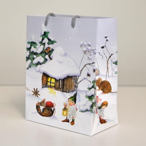 Könnte beinhalten: Rechteckige Geschenktüte mit einer Illustration einer Winterszene. Die Tasche zeigt eine schneebedeckte Hütte, eine Maus und Zwerge. Der Hintergrund ist eine verschneite Landschaft mit Kiefern und Schneeflocken. Die Tasche hat graue Kordelgriffe.