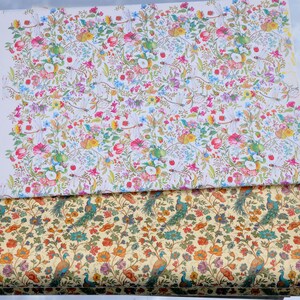 Könnte beinhalten: Zwei Stoffrollen mit Blumen- und Pfauenmustern. Die obere Rolle hat einen weißen Hintergrund mit einem farbenfrohen Blumendesign. Die untere Rolle hat einen beigefarbenen Hintergrund mit Pfauen- und Blumenmotiven.