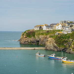 Może przedstawiać: Malownicze nadmorskie miasteczko z kolorowymi łodziami rybackimi zacumowanymi w porcie. Miasteczko jest zbudowane na klifie z widokiem na ocean.