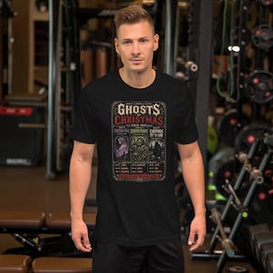 Pode incluir: Uma t-shirt preta de manga curta com uma estampa gráfica intitulada Ghosts of Christmas Tour 1843. O design inclui três painéis retangulares que retratam espíritos, com texto listando datas e locais, tudo dentro de uma moldura vintage.