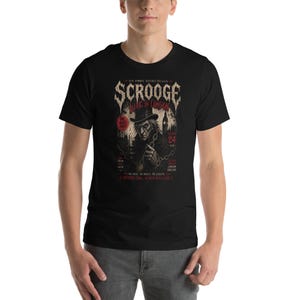 Pode incluir: T-shirt preto com um design vintage para "Scrooge Live in London". O gráfico inclui uma ilustração de uma figura com cartola, com texto e imagens que lembram um cartaz de concerto. A t-shirt é usada por uma pessoa.