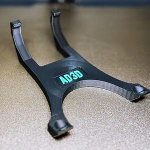 May include: A black 3D-printed stand with a curved design. The stand has a central platform with the text "AD3D" in teal. The stand has two curved arms extending upwards and two feet.