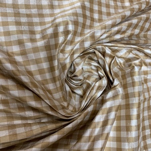 May include: A close-up of a beige and white gingham fabric. The fabric is woven with a subtle sheen and has a soft, drapey texture.