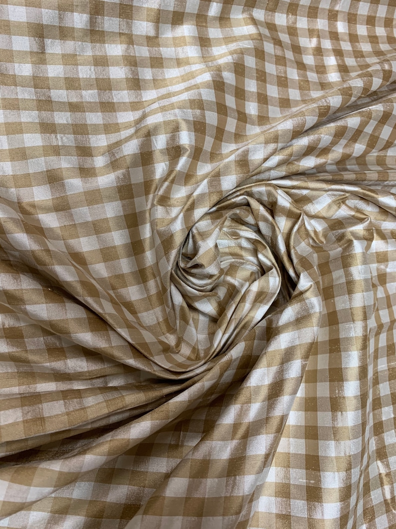 May include: A close-up of a beige and white gingham fabric. The fabric is woven with a subtle sheen and has a soft, drapey texture.