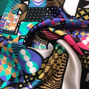 May include: A colorful silk scarf with a geometric pattern. The scarf features a variety of shapes and colors, including black, white, gold, teal, purple, and pink. The design includes polka dots, squares, and abstract shapes.
