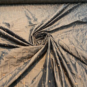 May include: A roll of dark grey fabric with a subtle sheen. The fabric features a pattern of vertical lines and small, scattered dots in a lighter, contrasting colour. The fabric is gathered in a spiral, showcasing its texture and drape.