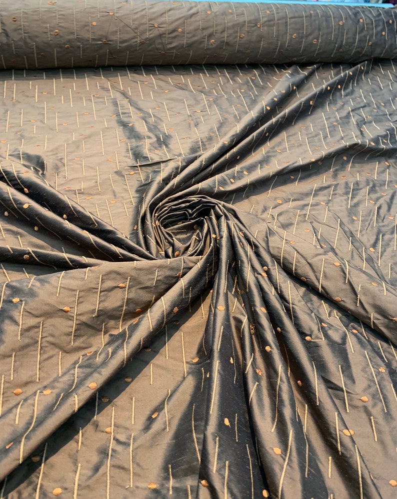 May include: A roll of dark grey fabric with a subtle sheen. The fabric features a pattern of vertical lines and small, scattered dots in a lighter, contrasting colour. The fabric is gathered in a spiral, showcasing its texture and drape.