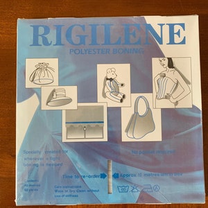 K&ouml;nnte beinhalten: Eine blaue Box mit dem Text "RIGILENE POLYESTER BONING" auf der Vorderseite. Die Box zeigt verschiedene M&ouml;glichkeiten, die Bonierung zu verwenden, darunter einen Hut, einen Teddyb&auml;r, eine Tasche und ein Korsett. Die Box enth&auml;lt auch Pflegehinweise und Informationen &uuml;ber den Inhalt, der 46 Meter oder 50 Yards Bonierung umfasst.