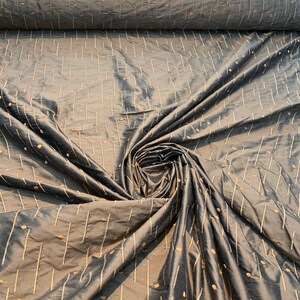 May include: Dark grey fabric with a subtle sheen, patterned with vertical lines and scattered dots in a lighter, golden-brown colour. The fabric is gathered in a swirl, showing its texture and drape.