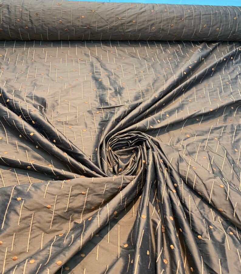 May include: Dark grey fabric with a subtle sheen, patterned with vertical lines and scattered dots in a lighter, golden-brown colour. The fabric is gathered in a swirl, showing its texture and drape.