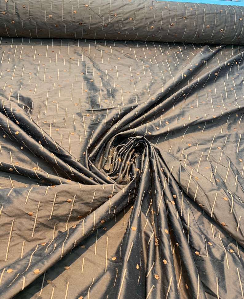 May include: A dark grey fabric with a sheen, patterned with vertical lines and scattered dots in a lighter colour. The fabric is draped, showing folds and texture, suggesting it's a decorative textile, possibly for upholstery.