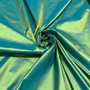 May include: A close-up of a teal green silk fabric with a slight sheen. The fabric is folded and draped, creating a soft, flowing texture.