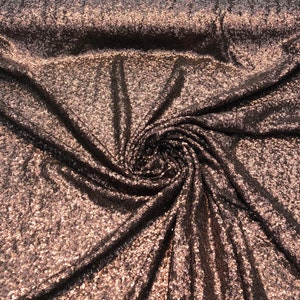 May include: Close-up of a brown and gold sequined fabric. The fabric is textured and has a shimmery finish.