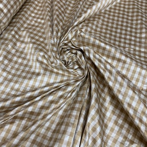 May include: A close-up of a white and gold gingham fabric. The fabric has a subtle sheen and is woven in a checkered pattern.