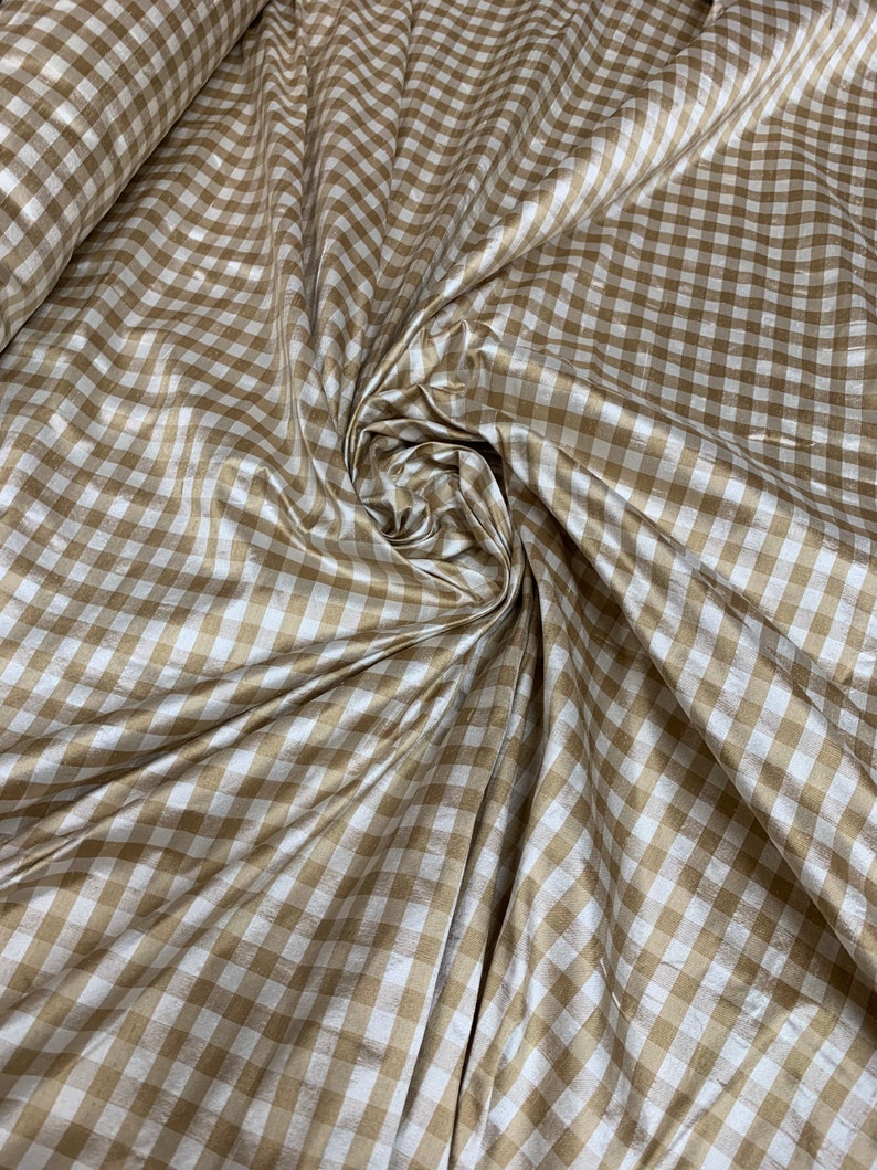 May include: A close-up of a white and gold gingham fabric. The fabric has a subtle sheen and is woven in a checkered pattern.