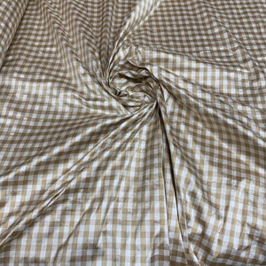 May include: A brown and white gingham fabric with a subtle sheen. The fabric is folded and draped, showing the texture and pattern.
